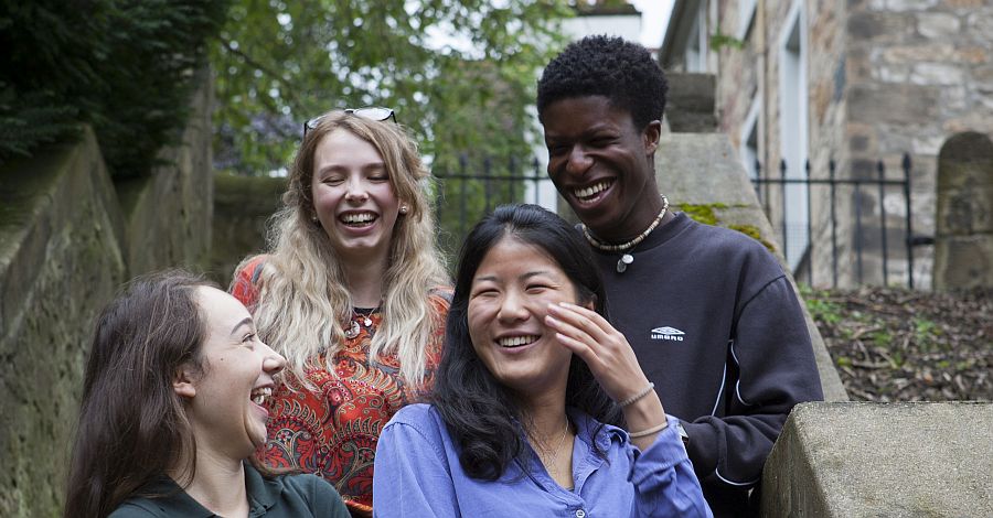 Close up of four Divinity students laughing together outside on the steps in New College garden